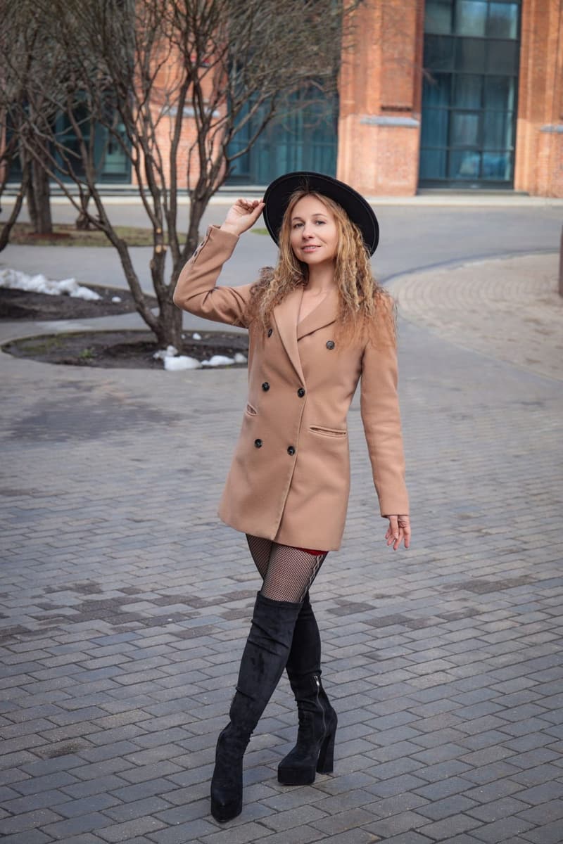 Woman in a camel double-breasted coat and a black wide-brim hat, hand on the brim