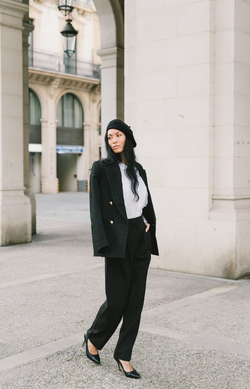 Woman in a black blazer and trousers with a beret, standing on a street
