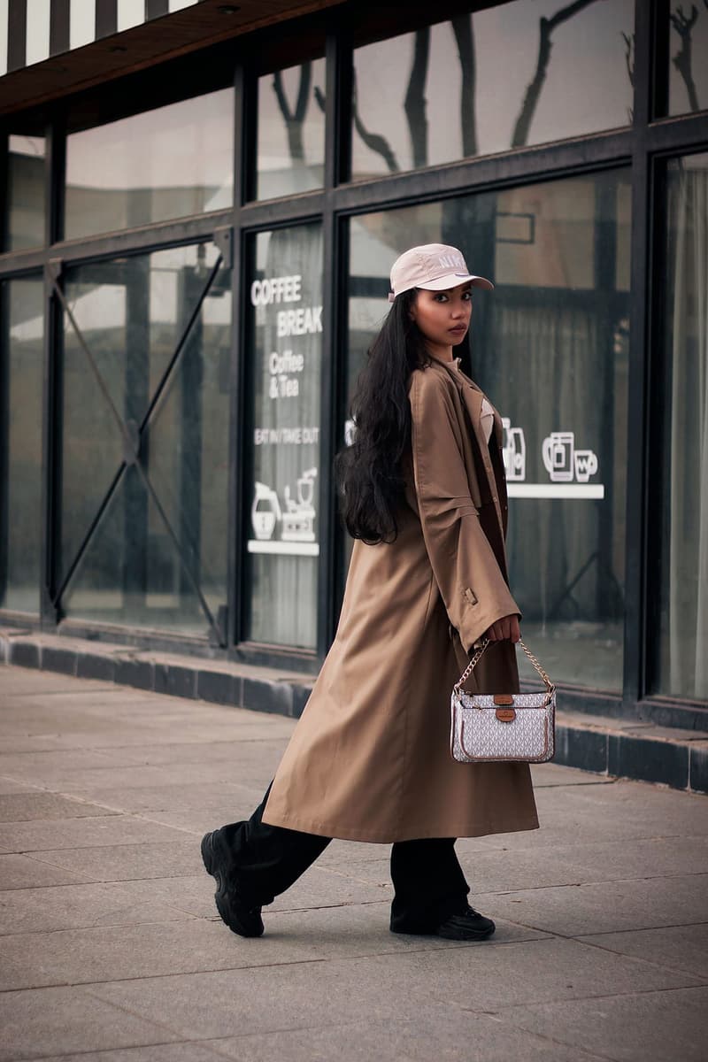 Woman in a long camel coat and a cap, carrying a small bag, on the pavement
